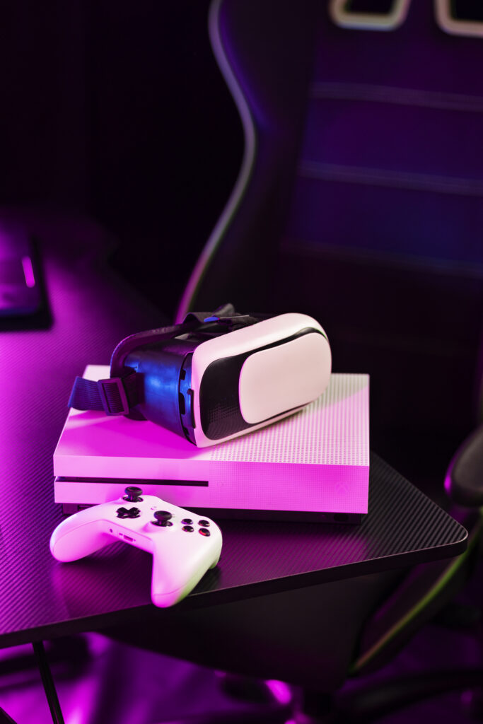 Consola Xbox blanca con control y dispositivo de realidad virtual en una mesa de juego iluminada con luces de neón. Compra en TechPlug CR